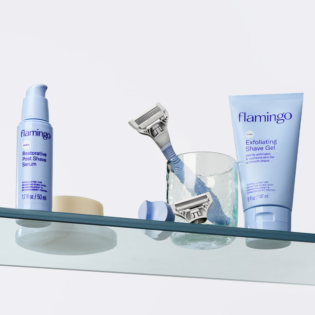 Flamingo's pubic razor, clear shave gel, and post-shave serum pictured on a glass shelf